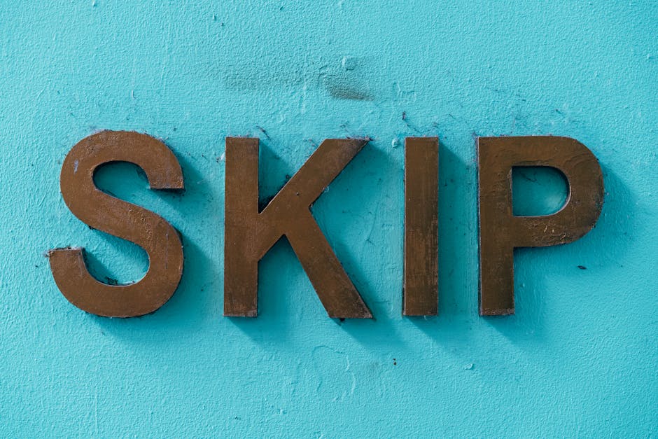 A close-up view of three large, uppercase metallic letters spelling 'SKIP' mounted on a bright turquoise textured wall. The letters have a matte, weathered finish with visible rust and wear, and are p